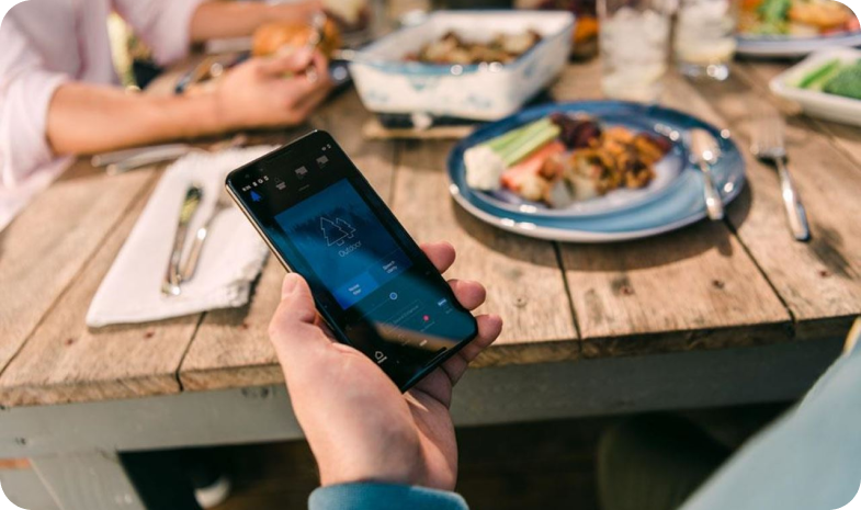 A man holds his smartphone, streaming audio from his hearing aid while enjoying an outdoor meal with friends.