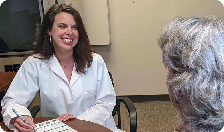 A Beltone hearing aid specialist talks with a patient. The doctor is smiling while filling out paperwork.