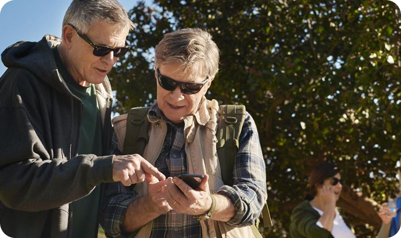 An older couple pause from a nature hike to look at a smartphone.