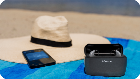 The Beltone Achieve hearing aid system is pictured laid out on a beach towel, next to a smart phone and a sun hat.