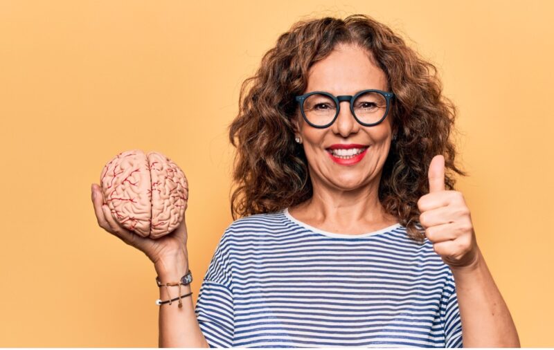 Smiling woman holding a plastic brain with a thumbs up
